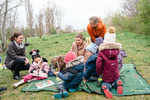 Eine Gruppe von Erwachsenen und Kindern sitzt auf einer Decke im Freien und interagiert spielerisch miteinander.