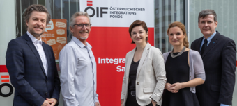 Fünf Personen stehen vor einem Banner des Österreichischen Integrationsfonds und lächeln.