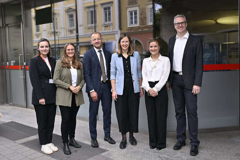 Sechs Personen stehen vor einem Gebäude und lächeln in die Kamera.