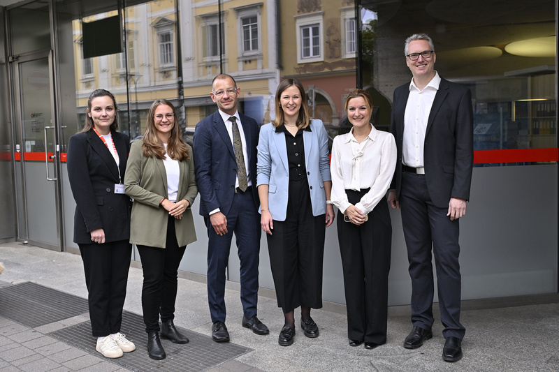 Sechs Personen stehen vor einem Gebäude und lächeln in die Kamera.