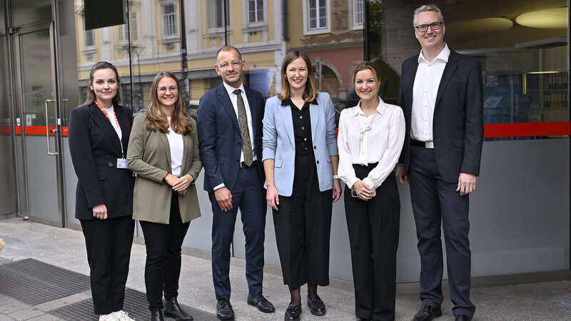 Sechs Personen stehen vor einem Gebäude und lächeln in die Kamera.