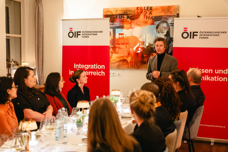 Ein Mann spricht vor Gästen bei einem Abendessen über Integration in Österreich.