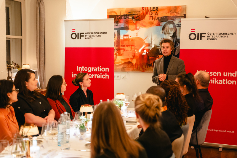 Ein Mann spricht vor Gästen bei einem Abendessen über Integration in Österreich.