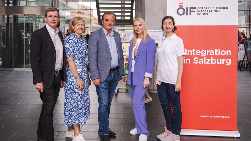 Fünf Personen stehen neben einem Banner mit dem Text „Integration in Salzburg“.