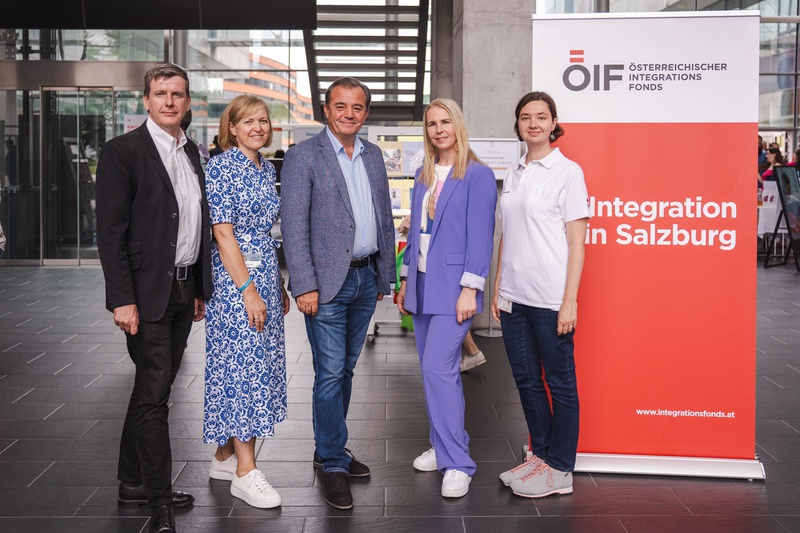 Fünf Personen stehen neben einem Banner mit dem Text „Integration in Salzburg“.