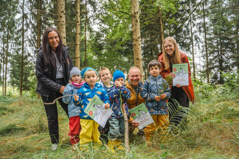 Eine Gruppe von Kindern und Erwachsenen steht im Wald und hält Urkunden in der Hand.