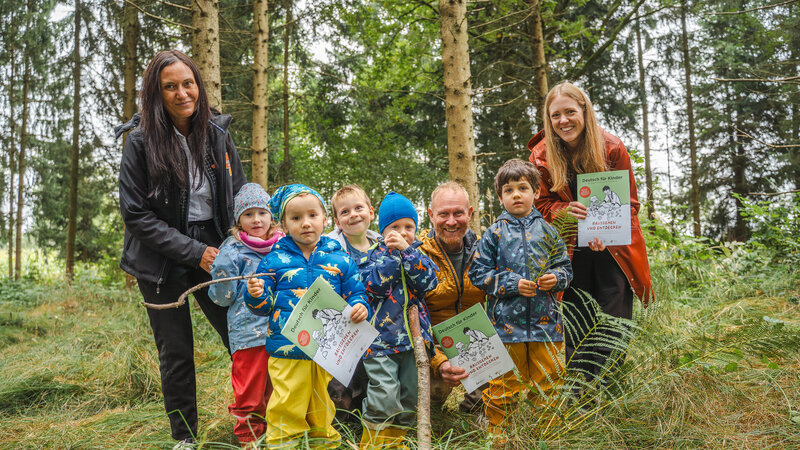 Eine Gruppe von Kindern und Erwachsenen steht im Wald und hält Urkunden in der Hand.