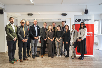 Eine Gruppe von zwölf Personen steht in einem Raum neben einem Banner des Österreichischen Integrationsfonds.