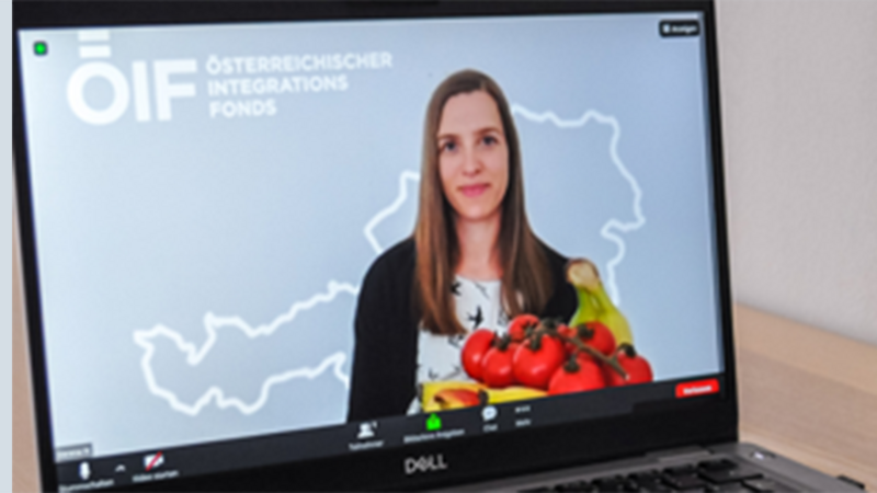 Eine Frau hält Obst, während sie vor einem Bildschirm mit einem Logo steht.
