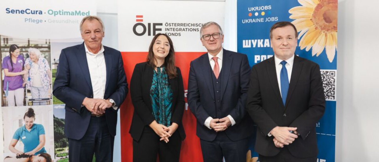 Vier Personen stehen zusammen vor Banner mit Logos und Texten zu Integrationsprojekten und Jobmöglichkeiten.