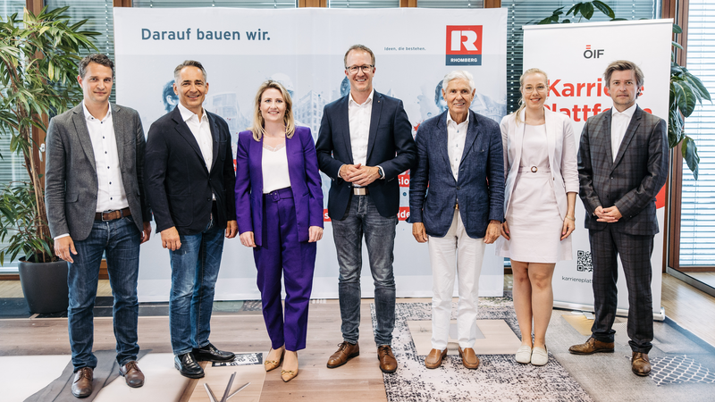 Sieben Personen stehen gemeinsam vor einem Banner mit den Worten „Darauf bauen wir“.
