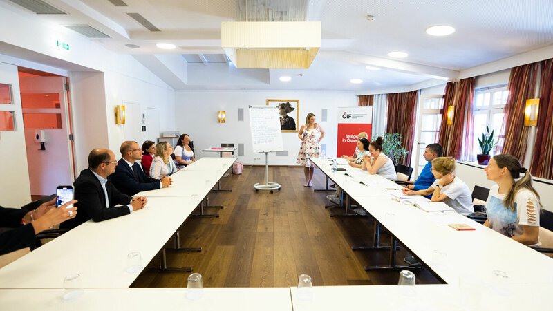 Eine Präsentation in einem Raum mit mehreren Teilnehmern, die einem Vortrag zuhören und Notizen machen.