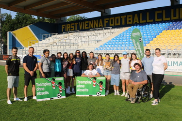 Gruppenfoto von Jugendlichen und Betreuern mit zwei Schildern, die "Teamplay ohne Abseits" in einem Fußballstadion zeigen.