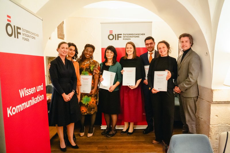 Eine Gruppe von Menschen hält Urkunden in der Hand, steht zusammen vor einem Banner des Österreichischen Integrationsfonds.