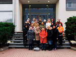 Gruppenfoto von Frauen und einem Mann vor einem Gebäude, alle lächeln und tragen warme Kleidung.