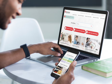 Ein Mann nutzt einen Laptop und ein Smartphone, um Informationen über Deutschkurse zu suchen.