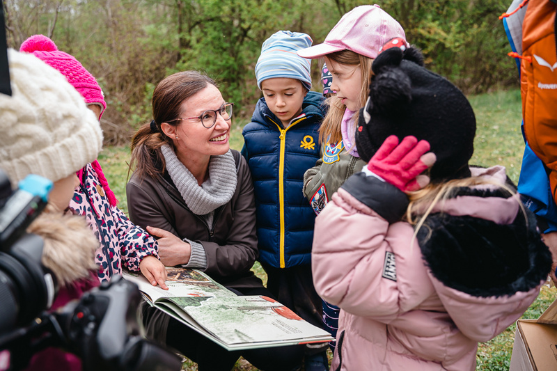 Eine Frau liest Kindern aus einem Bilderbuch vor, während sie aufmerksam zuhören.