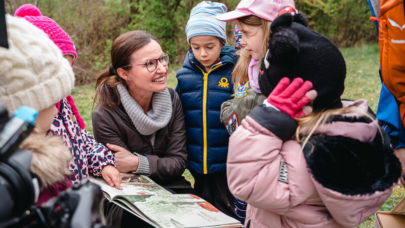 Eine Frau liest Kindern aus einem Bilderbuch vor, während sie aufmerksam zuhören.