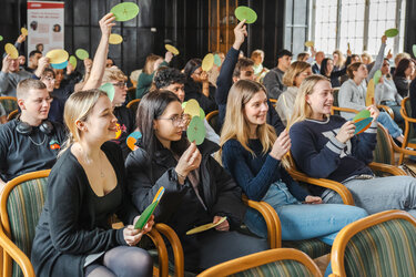 Teilnehmer heben in einem Saal grüne Karten, um ihre Meinungen während einer Veranstaltung auszudrücken.