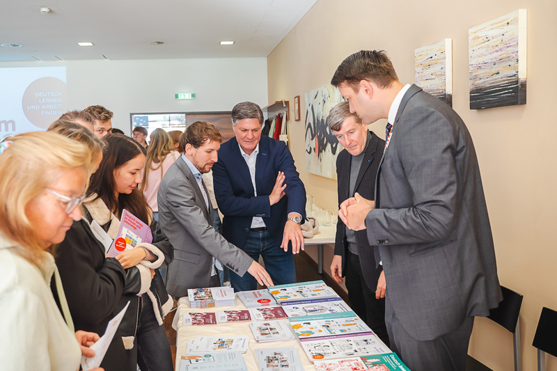 Eine Gruppe von Menschen betrachtet gemeinsam Informationsmaterialien auf einem Tisch während einer Veranstaltung.