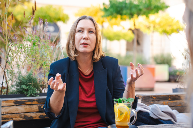 Eine Frau mit kurzem Haarschnitt spricht gestikulierend, während sie ein Getränk mit Zitronen und Kräutern vor sich hat.