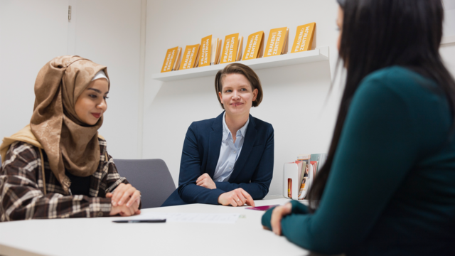 Drei Frauen sitzen an einem Tisch in einem Büro und führen ein Gespräch.