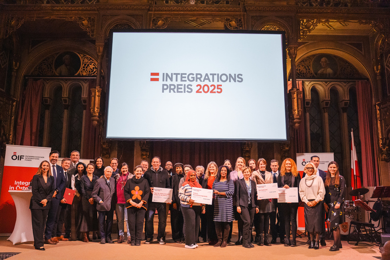 Gruppenfoto von Preisträgern des Integrationspreises 2025 vor einer großen Leinwand mit dem Preisnamen.