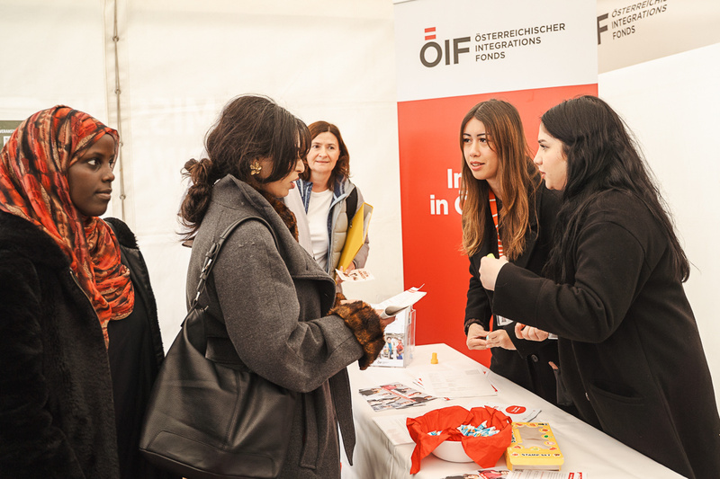 Menschen stehen an einem Tisch des Österreichischen Integrationsfonds, während Informationen ausgetauscht werden.