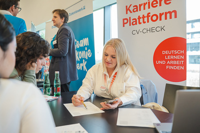 Eine Frau berät Teilnehmer an einem Tisch und notiert Informationen für Karriereangebote.