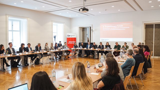 Eine Gruppe von Menschen nimmt an einem Forum in einem Konferenzraum teil. Tische sind in U-Form angeordnet.