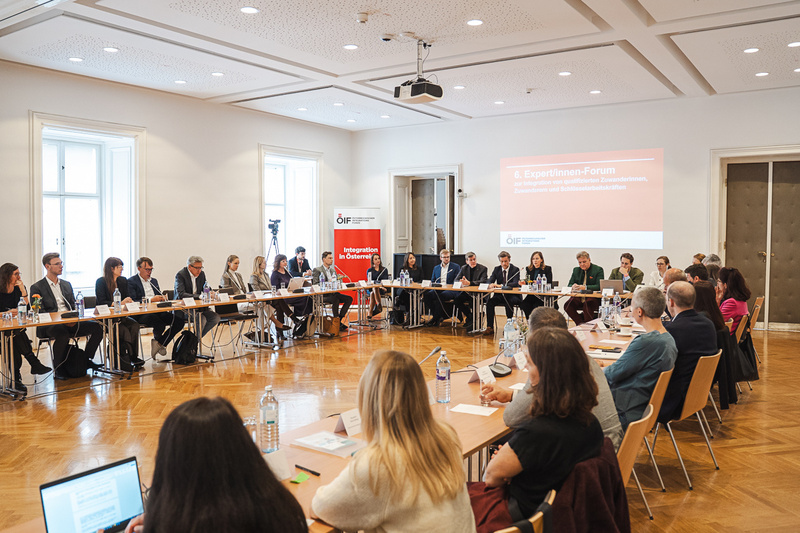 Eine Gruppe von Menschen nimmt an einem Forum in einem Konferenzraum teil. Tische sind in U-Form angeordnet.