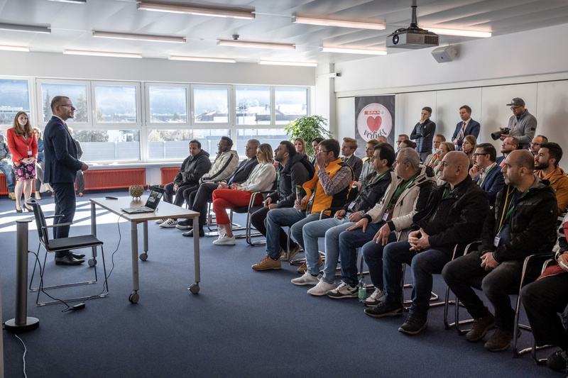 Eine Person spricht, während eine Gruppe von Zuhörern im Raum aufmerksam zuhört.