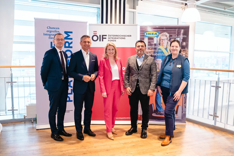 Fünf Personen stehen nebeneinander vor Werbebannern für Integrationsprojekte und Arbeitsmöglichkeiten.