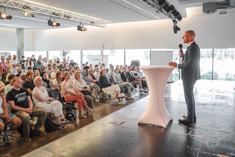 Sprecher am Rednerpult präsentiert vor sitzendem Publikum in modernem Raum