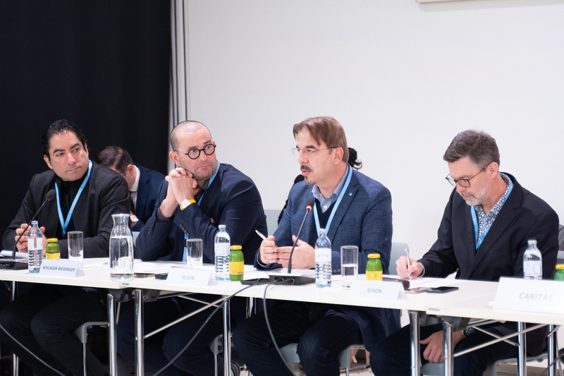 Vier Männer sitzen an einem Tisch und diskutieren während einer Tagung.