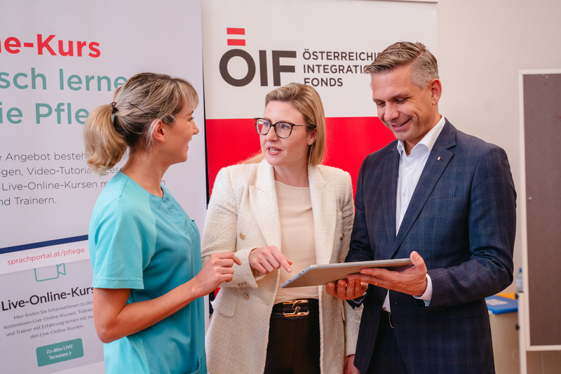 Drei Personen unterhalten sich und betrachten gemeinsam ein Tablet, während ein Banner im Hintergrund sichtbar ist.