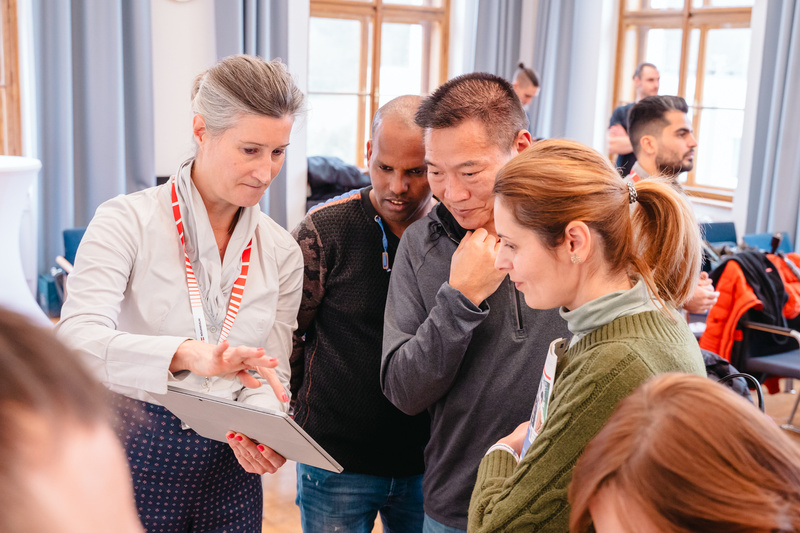 Eine Gruppe von Personen schaut auf ein Tablet und diskutiert aufmerksam miteinander.