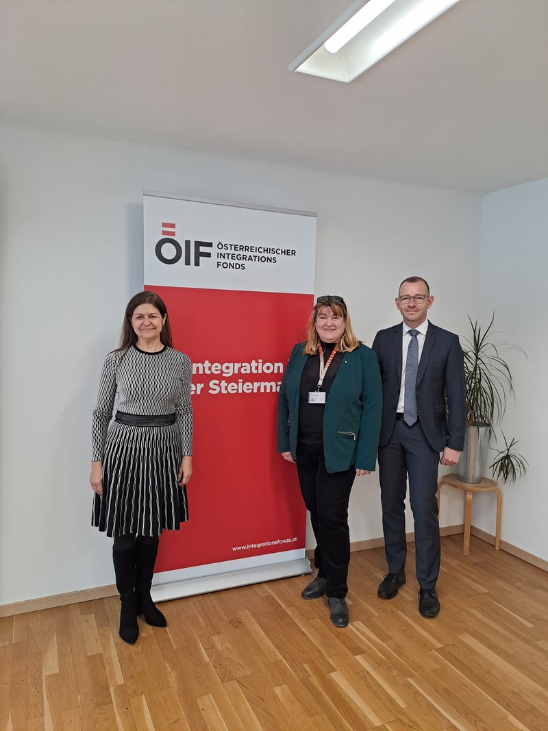 Drei Personen stehen vor einem Banner des Österreichischen Integrationsfonds in einem hellen Raum.