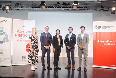 Eine Gruppe von fünf Personen steht auf einer Bühne, umgeben von Informationsplakaten zu Karriere und Integration.