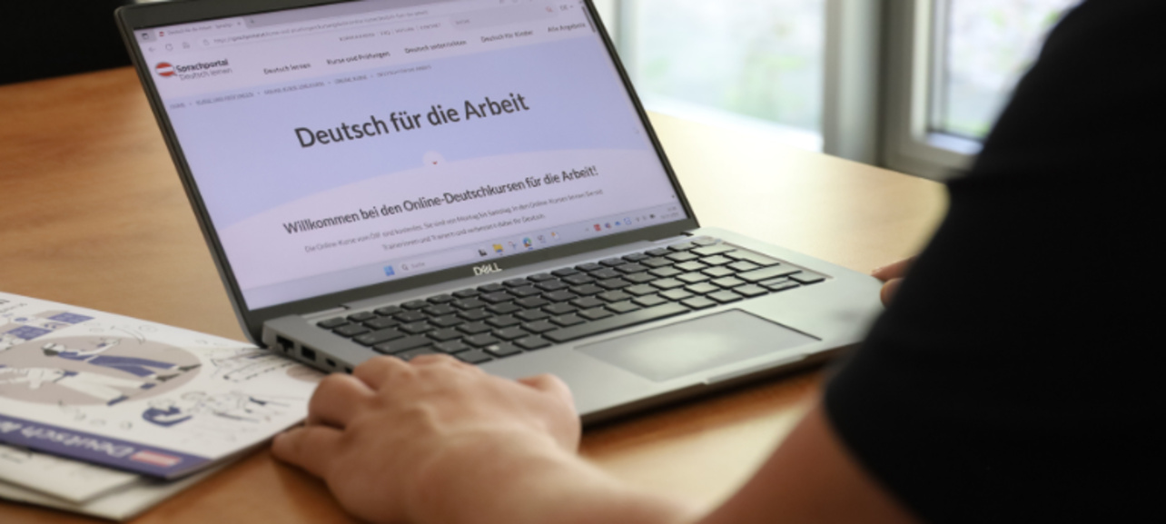 Laptop auf einem Tisch zeigt die Webseite "Deutsch für die Arbeit" mit Online-Deutschkursen.