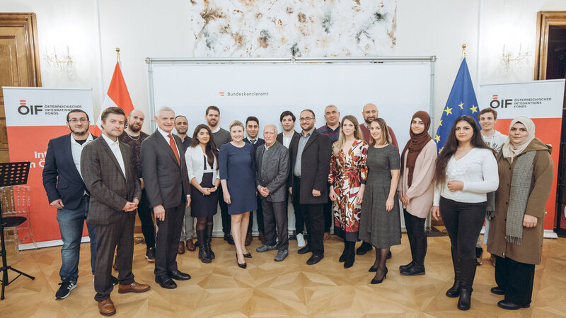 Gruppenfoto von Teilnehmern eines Integrationsprogramms im Bundeskanzleramt mit Flaggen im Hintergrund.