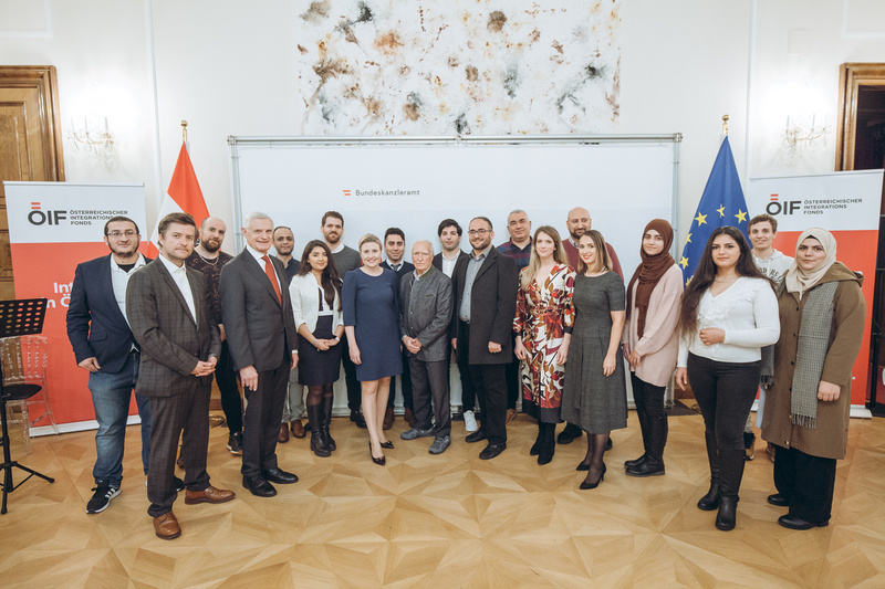 Gruppenfoto von Teilnehmern eines Integrationsprogramms im Bundeskanzleramt mit Flaggen im Hintergrund.