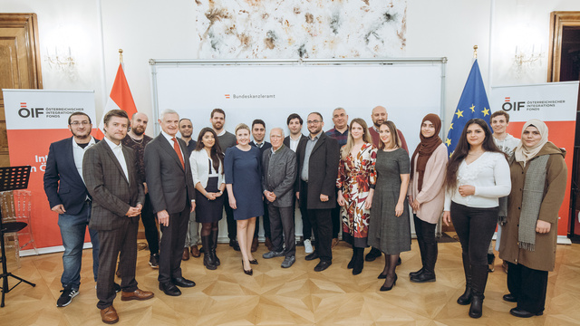 Gruppenfoto von Teilnehmern eines Integrationsprogramms im Bundeskanzleramt mit Flaggen im Hintergrund.