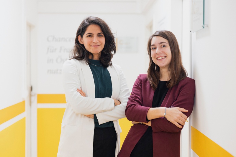 Zwei Frauen stehen lächelnd in einem Flur.