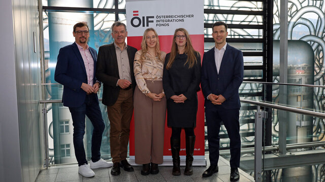 Fünf Personen stehen vor einem Banner des Österreichischen Integrationsfonds.