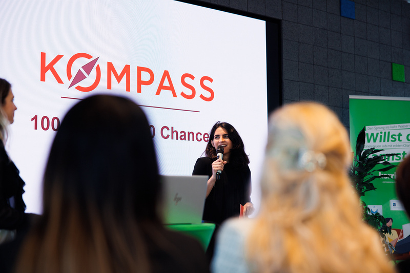 Eine Frau spricht auf einer Veranstaltung mit dem Titel "KOMPASS – 100 Chancen für 100 Chancen".