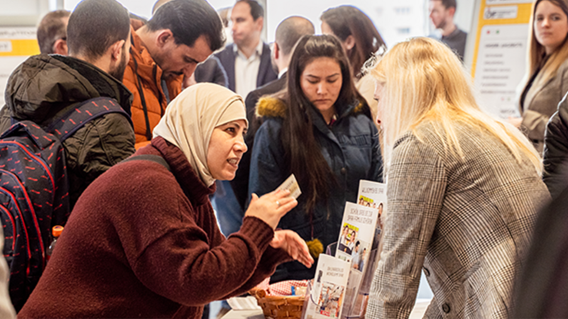 Eine Frau mit Kopftuch erklärt etwas leidenschaftlich einer anderen Frau an einem Informationsstand.