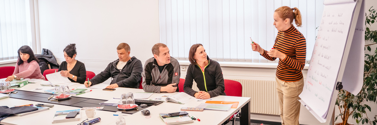 Eine Fraue steht vor einem Flipchart und erklärt einer Gruppe etwas