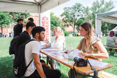 Zwei Beraterinnen sprechen mit jungen Leuten an einem Informationsstand im Freien.
