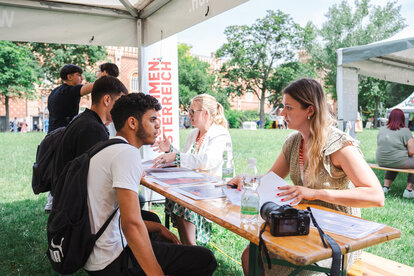 Zwei Beraterinnen sprechen mit jungen Leuten an einem Informationsstand im Freien.